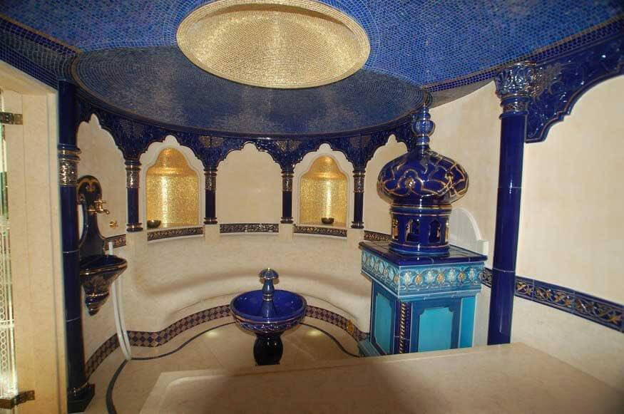 Das Hamam-Dampfbad ist mit einer halbrunden Sitzbank und einer Massageliege aus Naturstein ausgestattet und wird nach oben hin von einer doppelten Kuppeldecke überdacht. In den goldenen Nischen sieht die orientalische Badgestaltung kleine Lampen vor, die von dem Mosaik reflektiert werden und das Bad in goldenes Licht tauchen.